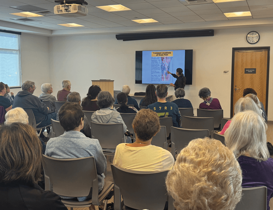 speaker pointing to a knee joint on a screen while attendees look on